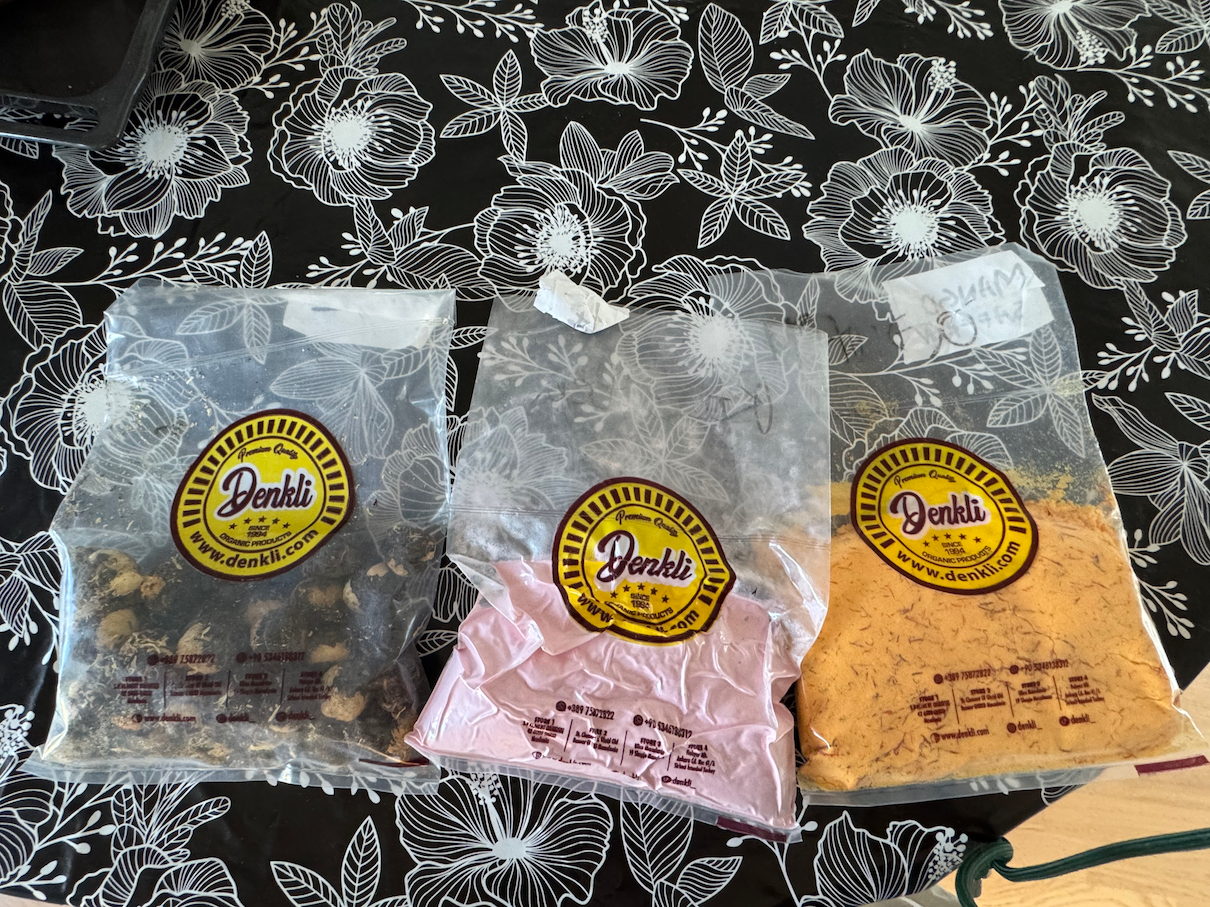 Three bags of Denkli brand organic spice powders and dried goods on a floral tablecloth.