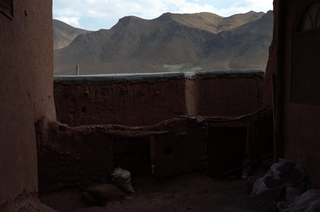 Red courtyard wall with mountains behind in Abyaneh