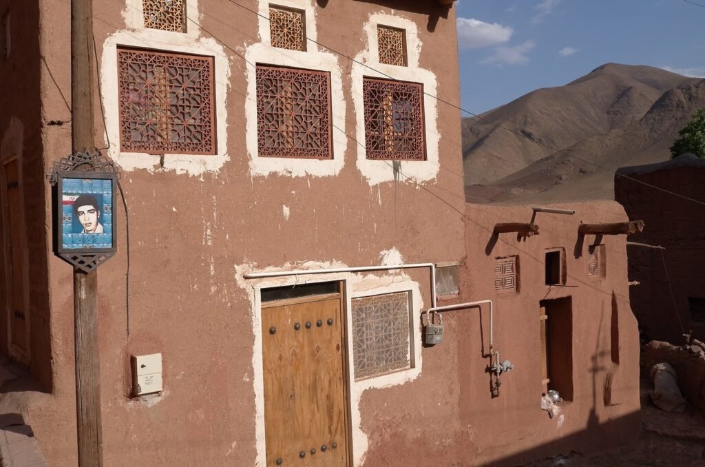 Red mud brick house with lattice windows and a wooden door in Abyaneh