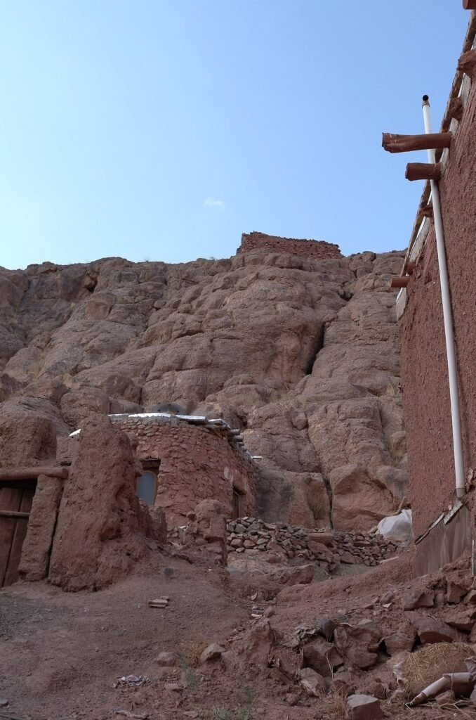 Ruined mud houses by a red rock face in Abyaneh
