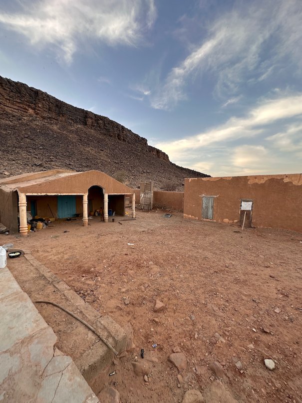A guesthouse with arches stands below a high rock cliff in the Adrar region.