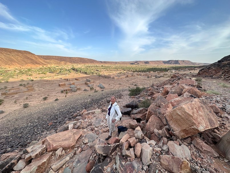 A man walks over large rocks in a wide desert valley in the Adrar region.