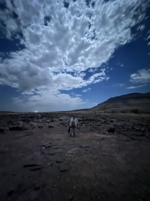 A man walks on rocky ground under bright night clouds in the Adrar region.