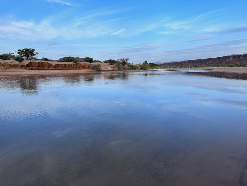 Calm water in a desert river reflects the blue sky and clouds.
