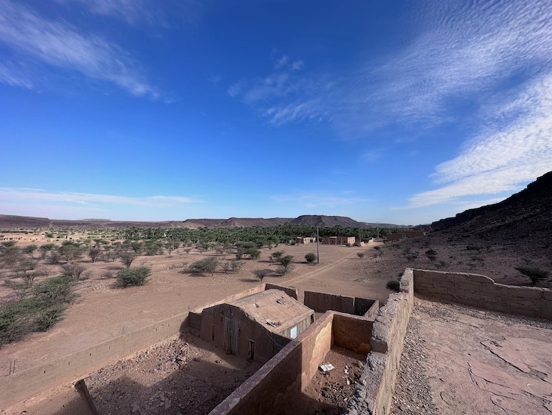 Mud brick houses and green trees lie in a valley under a blue sky in Adrar.
