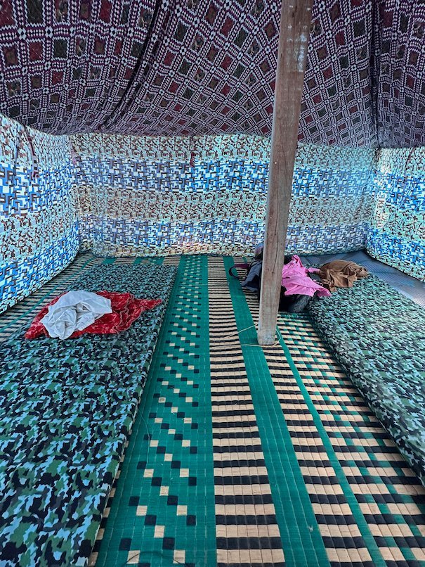 Colorful mats and fabric walls fill the inside of a large tent.
