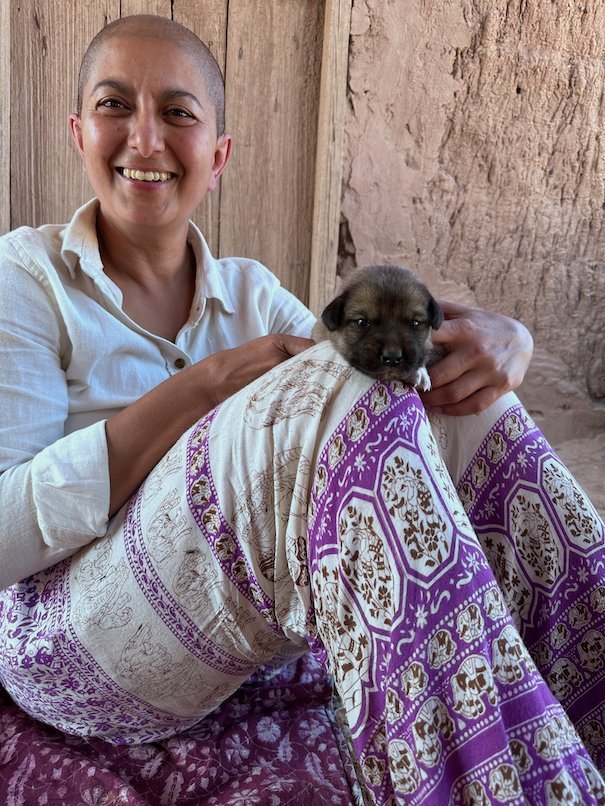 Zayera Khan smiles and holds a small puppy on her lap in the shade.