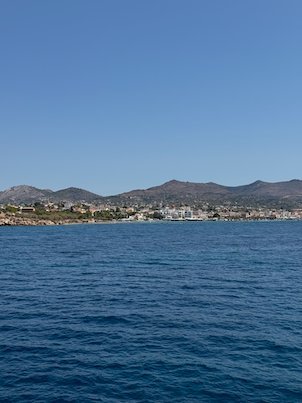 Coast of Aegina with white houses and hills, seen from the ferry