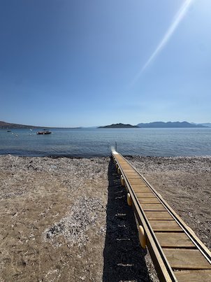 Long wooden jetty across a pebble beach to the calm sea in Aegina