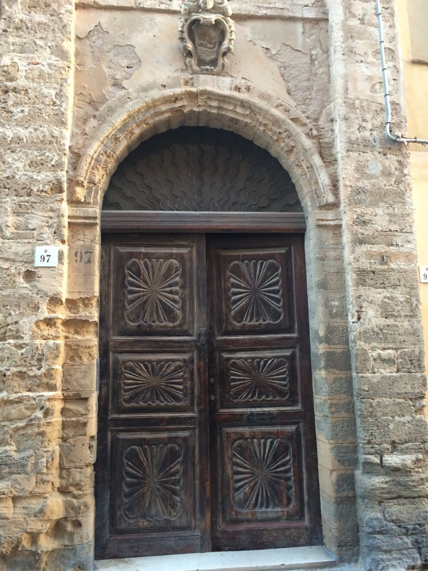A carved wooden door sits in an arched stone doorway in the old town of Alghero.
