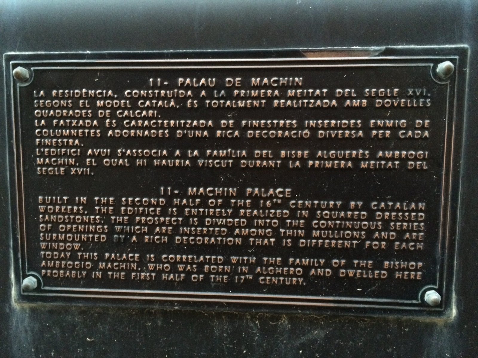 A metal plaque in Catalan and English tells the history of Machin Palace in Alghero.