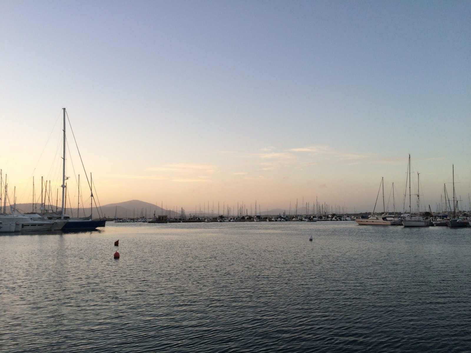 Sailboats lie in the marina of Alghero under a soft evening sky.