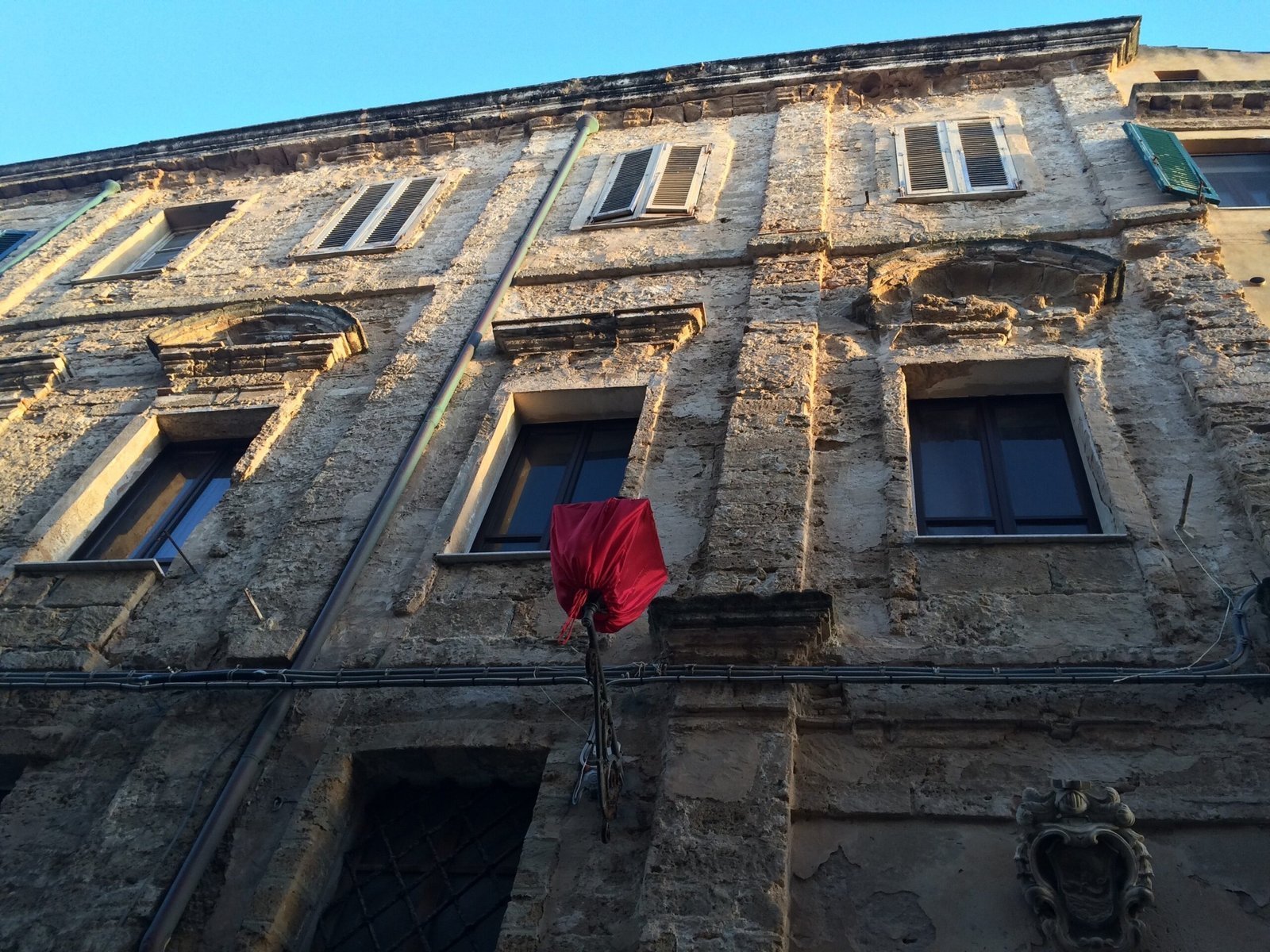 An old stone house with shutters stands on a narrow street in the old town of Alghero.