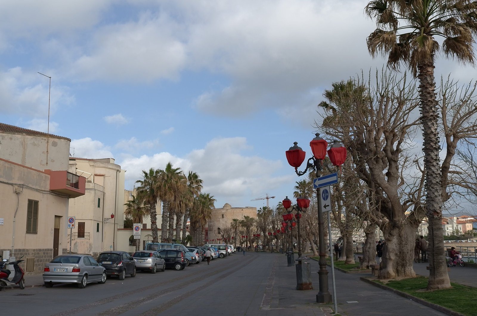 Palm trees and red street lamps line a street in Alghero in Sardinia.