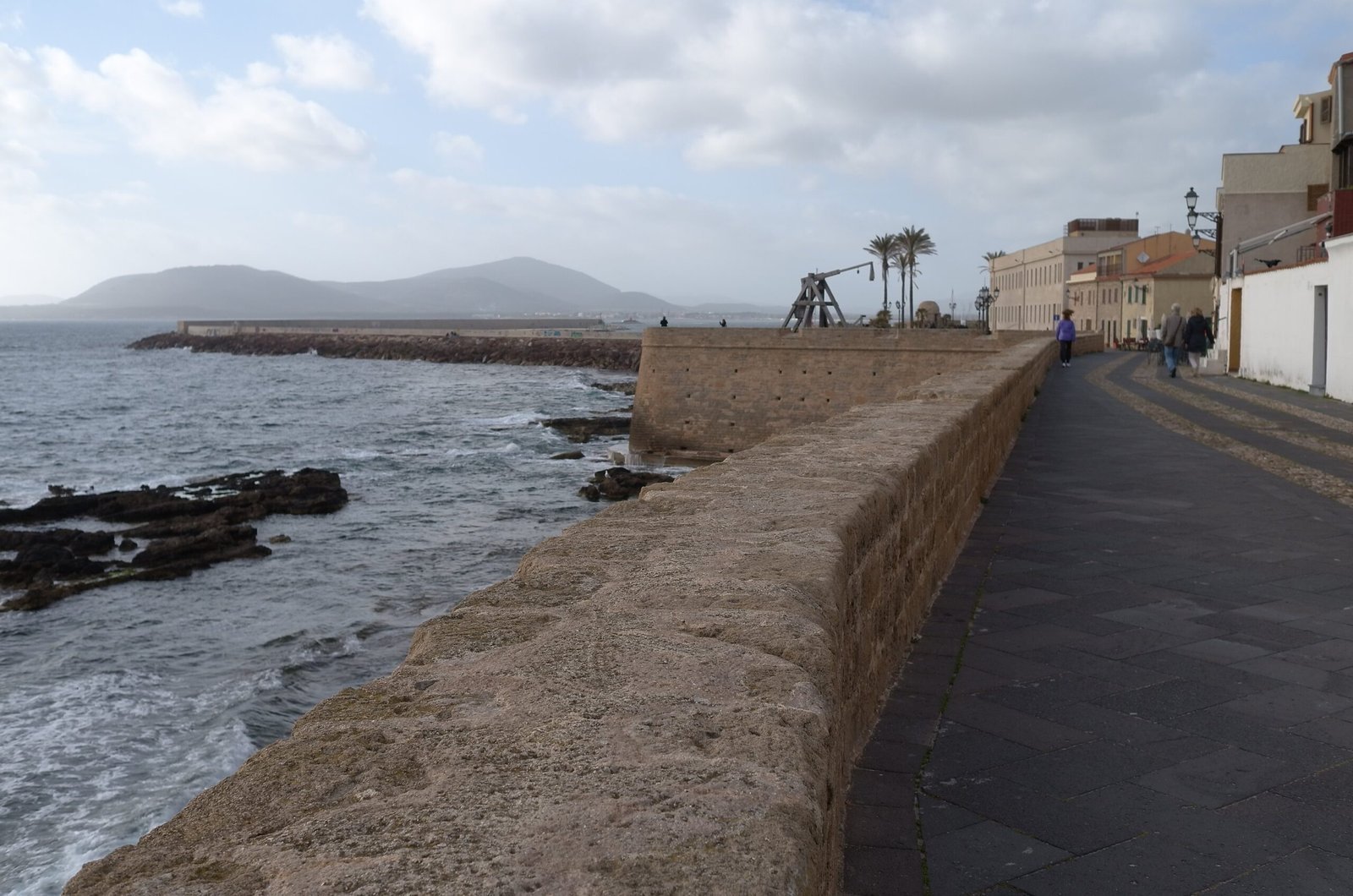 A walkway runs along the old sea wall above the rocks in Alghero.