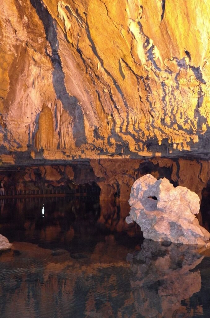 Underground lake with a white rock and orange light in Ali Sadr Cave