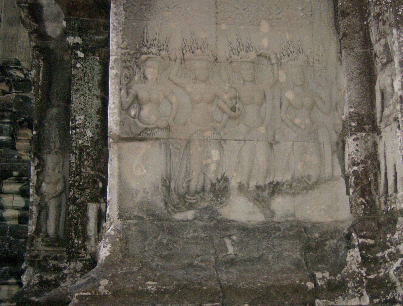 A carved relief panel with figures sits between stone pillars at an Angkor temple.