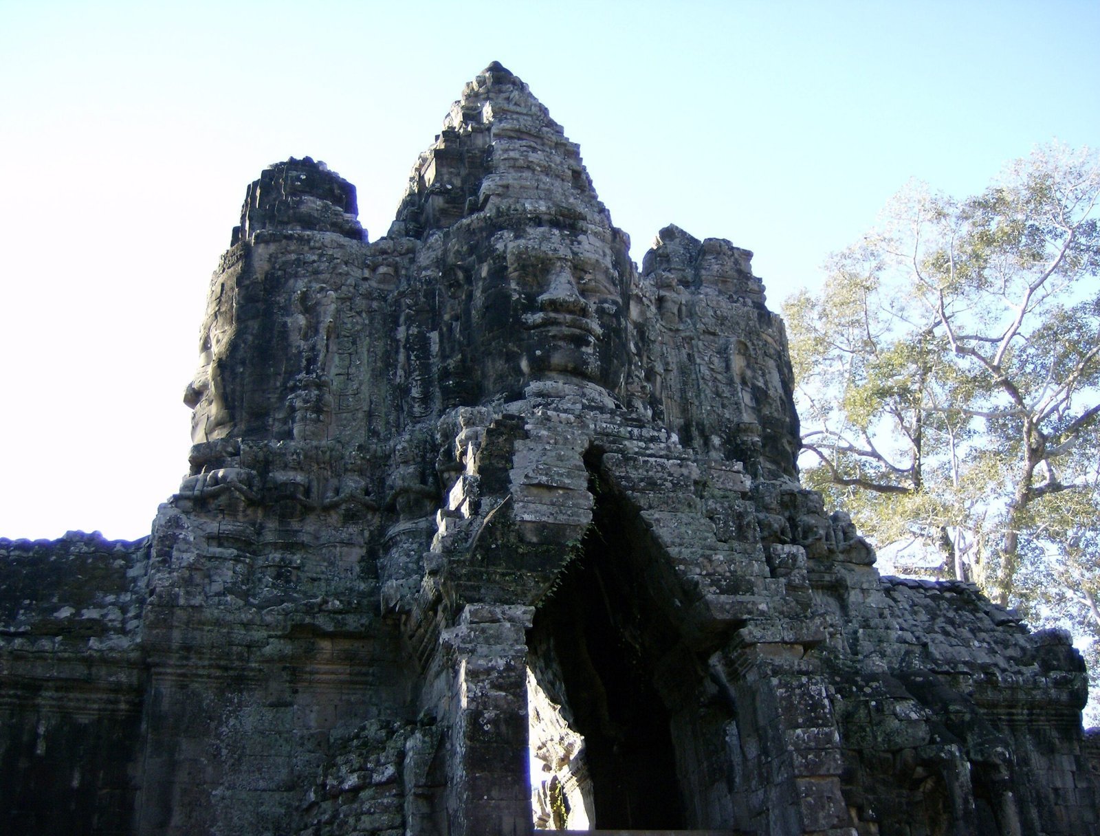 A stone gate tower with carved faces stands against a clear sky at Angkor Thom.