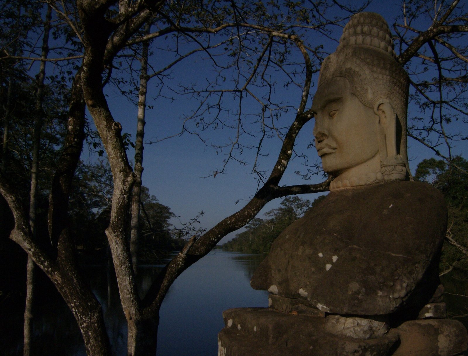 A stone guardian head looks over the moat at Angkor Thom at dusk.