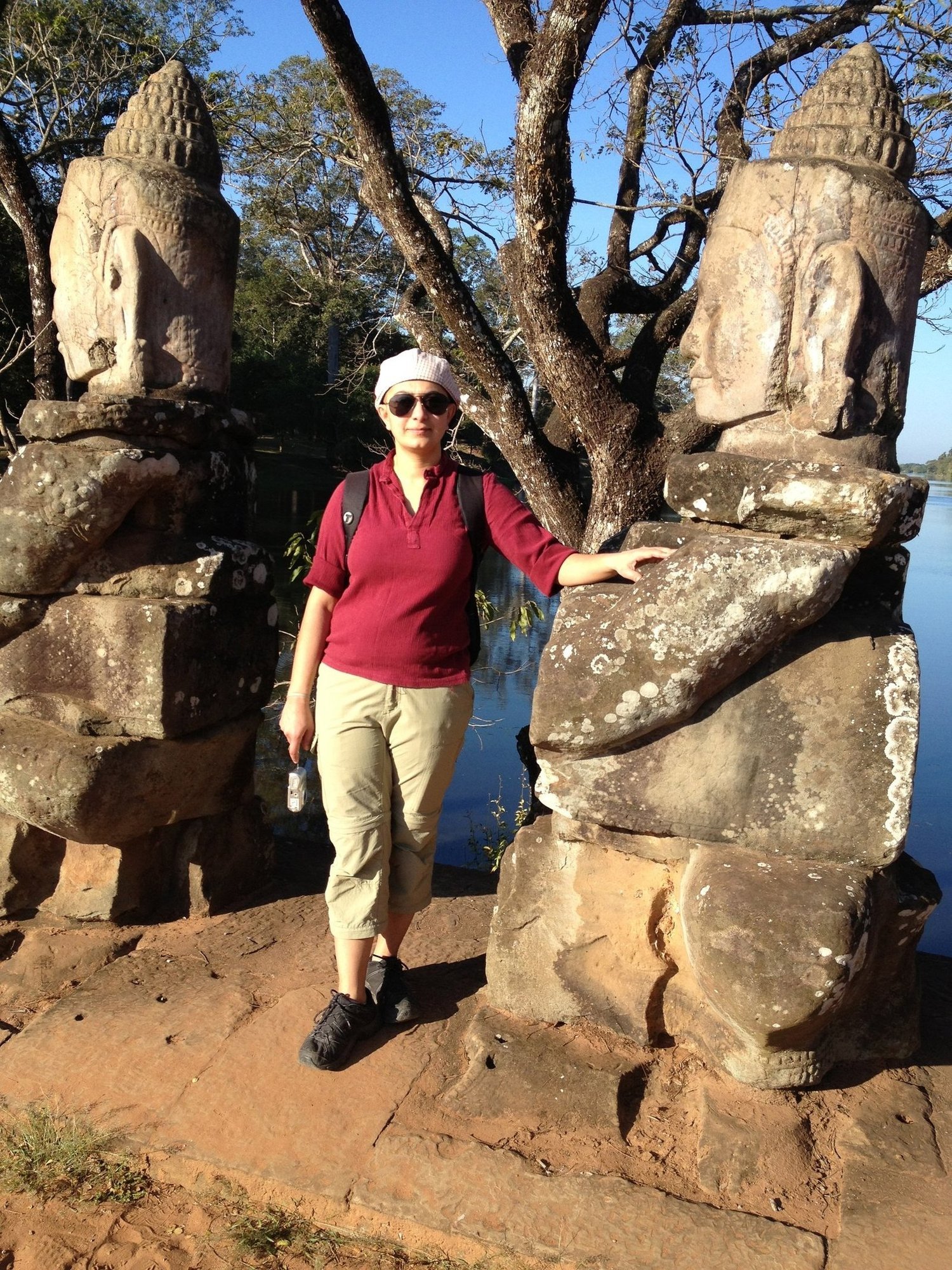 A traveler in a red shirt stands between stone guardians on the causeway at Angkor Thom.