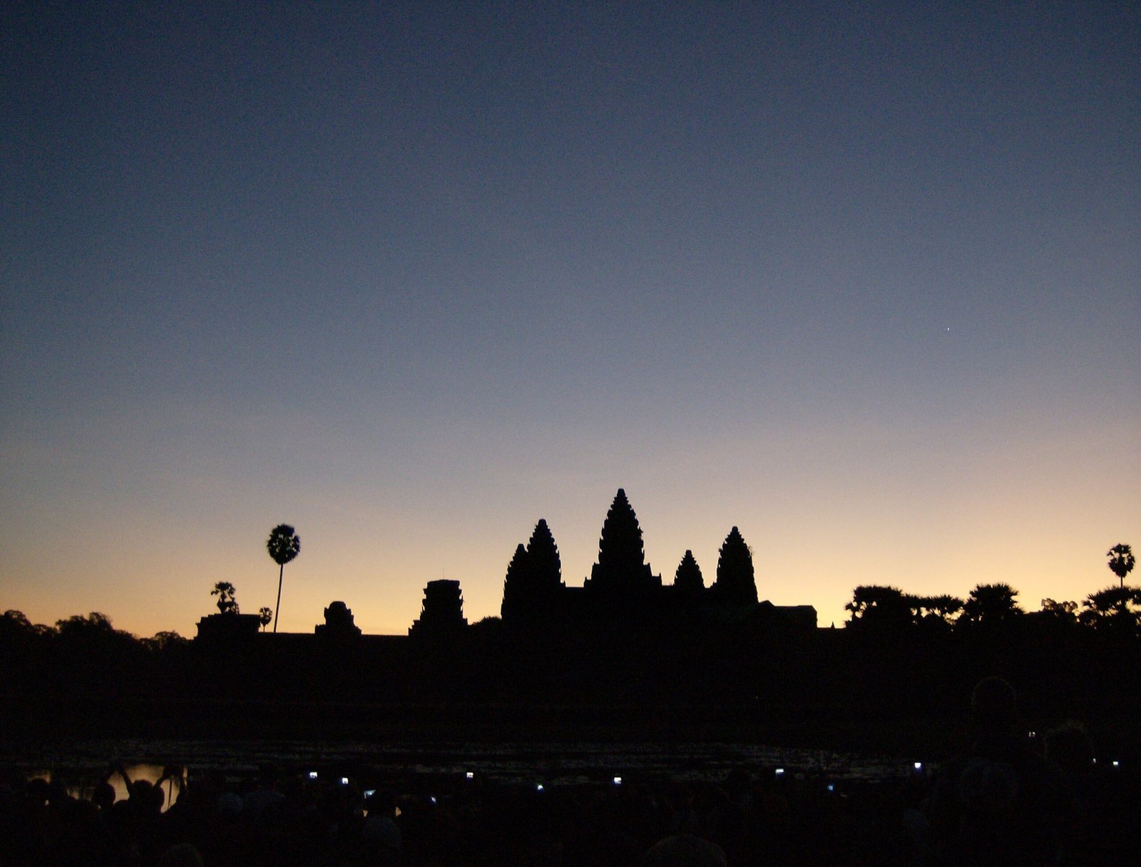 The towers of Angkor Wat show as a dark outline against the orange sky at sunrise.