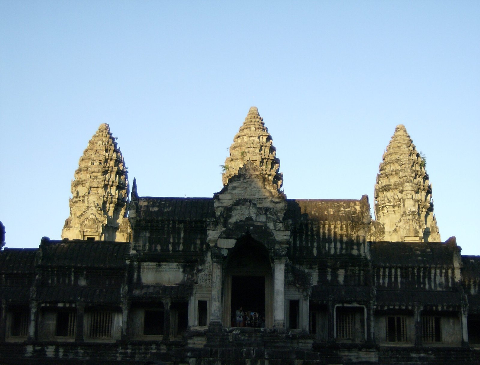 The three central towers of Angkor Wat rise above the outer gallery in late light.