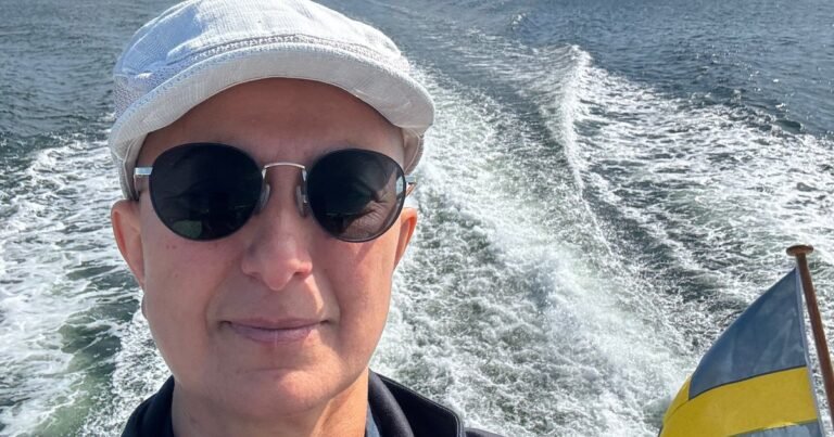 Zayera Khan in a white cap and sunglasses on a boat, with the wake and a Swedish flag behind her