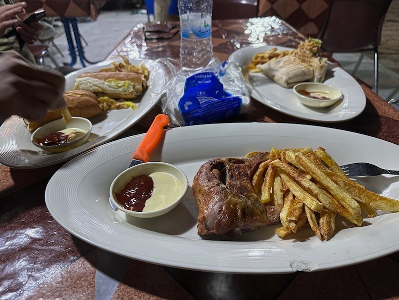 Plates of grilled chicken, fries and bread stand on a restaurant table.