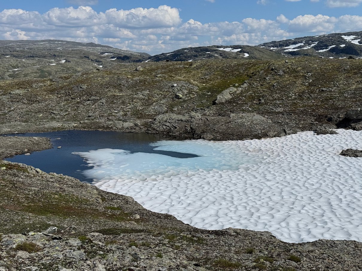 Small lake with ice and a large snowfield on the mountain plateau