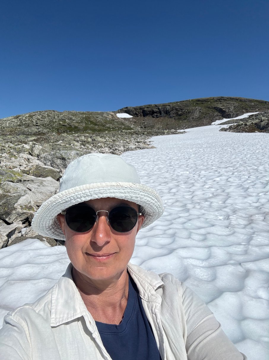 Selfie in a white sun hat in front of a snowfield in summer