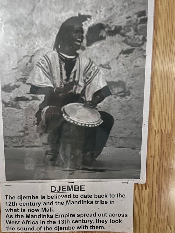 An old photo of a djembe player hangs with a text in the Kachikally museum, Bakau.