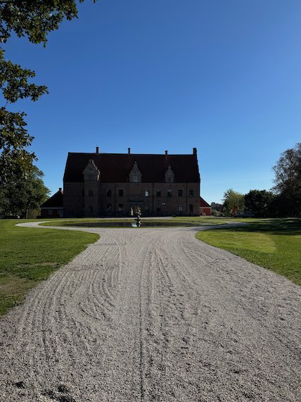 Dark brick castle with stepped gables at the end of a wide gravel drive and lawns