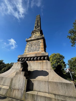 Close view of the Battle of Lund monument, a stone obelisk with a text plaque and cannonballs