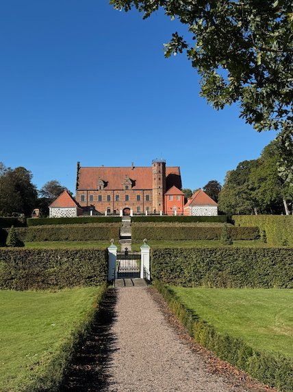 Red brick manor house at the end of a gravel path through a formal garden with clipped hedges