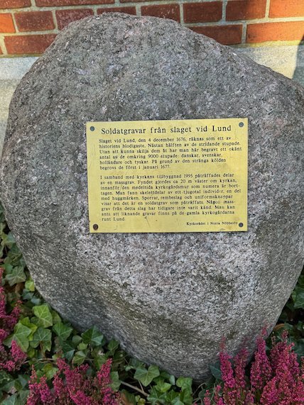 Large boulder with a brass plaque about the soldiers graves from the Battle of Lund, with heather in front