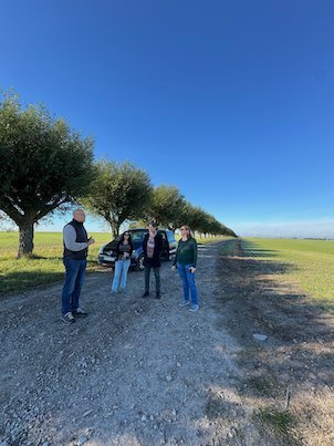 Three people standing on a gravel farm road beside a row of willows on the battlefield route