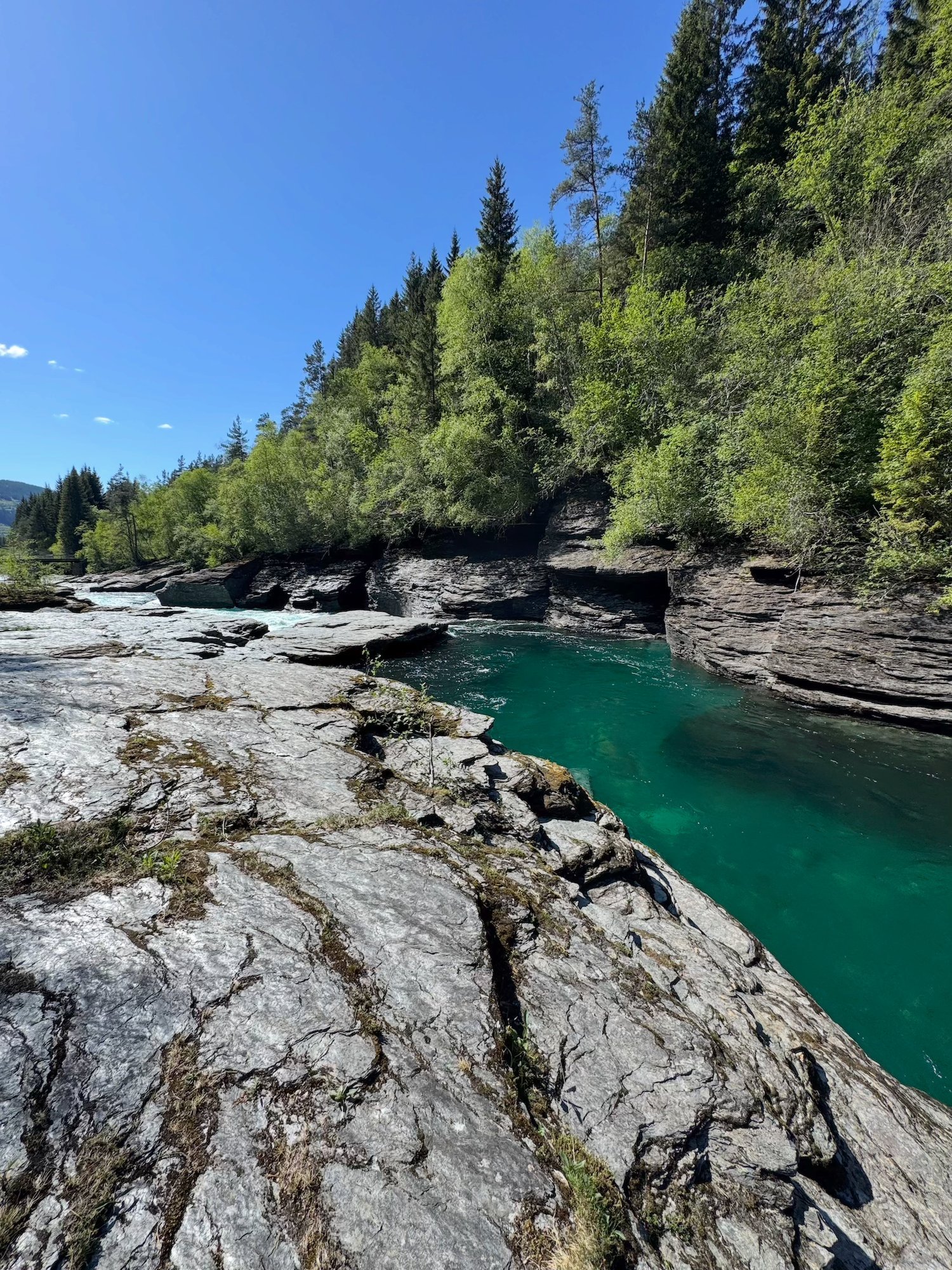 Calm green pool in the river between rock cliffs and birch trees at Bømoen