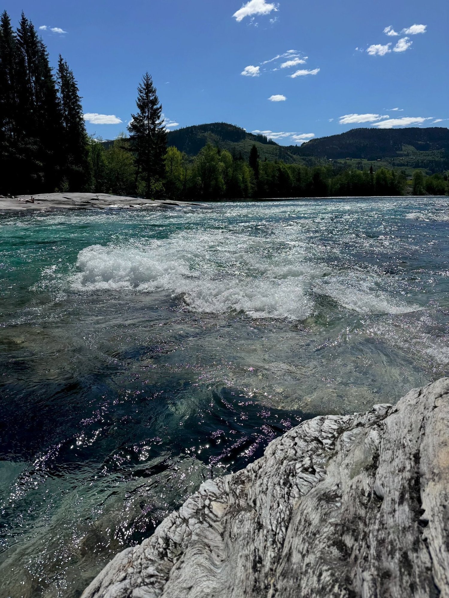 Turquoise river water that foams over rocks at Bømoen, with forest behind