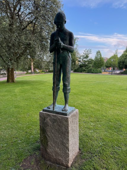 Bronze statue of a boy on a stone plinth in a park in Borås
