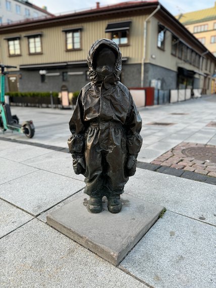 Bronze sculpture of a small child in a raincoat on a street in Borås