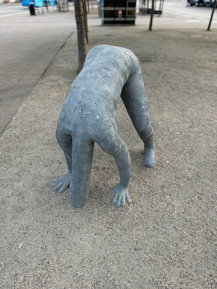 Grey sculpture of a crawling human figure on a pavement in Borås