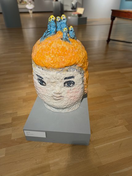 Ceramic head with orange hair and small blue birds on top
