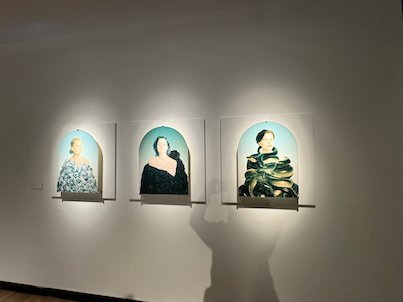 Three painted portraits of women in arched frames on a gallery wall