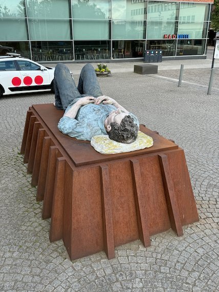 Sculpture of a man lying on a rusty steel bed on a street in Borås