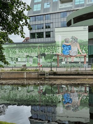 Mural of two people on a bench, reflected in the river in Borås