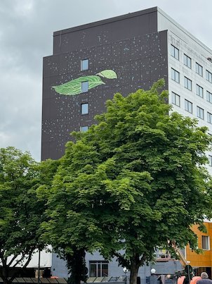 Mural of a green leaf on a dark tower building above green trees
