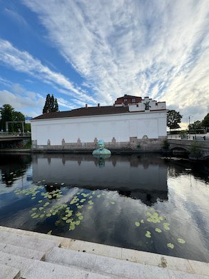 White museum building and a figure in the water, reflected in the river with water lilies