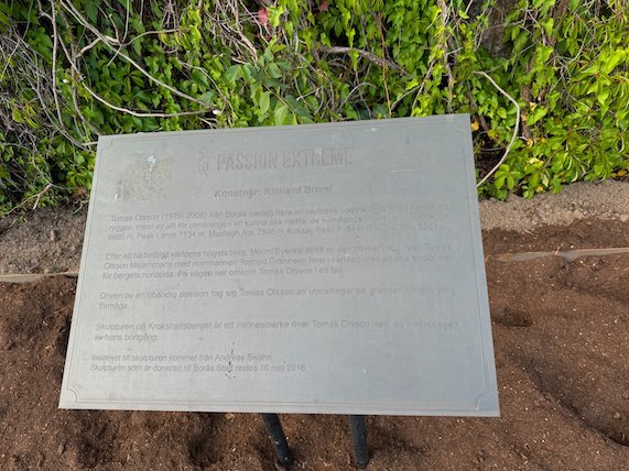 Metal plaque about a sculpture, on the ground among plants