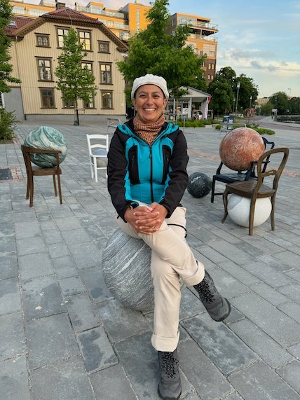Smiling person sits on a stone sphere in the artwork Les Sièges des Mondes