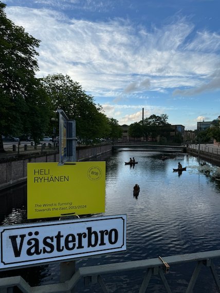 Västerbro sign and a yellow art sign Heli Ryhänen by the river in Borås
